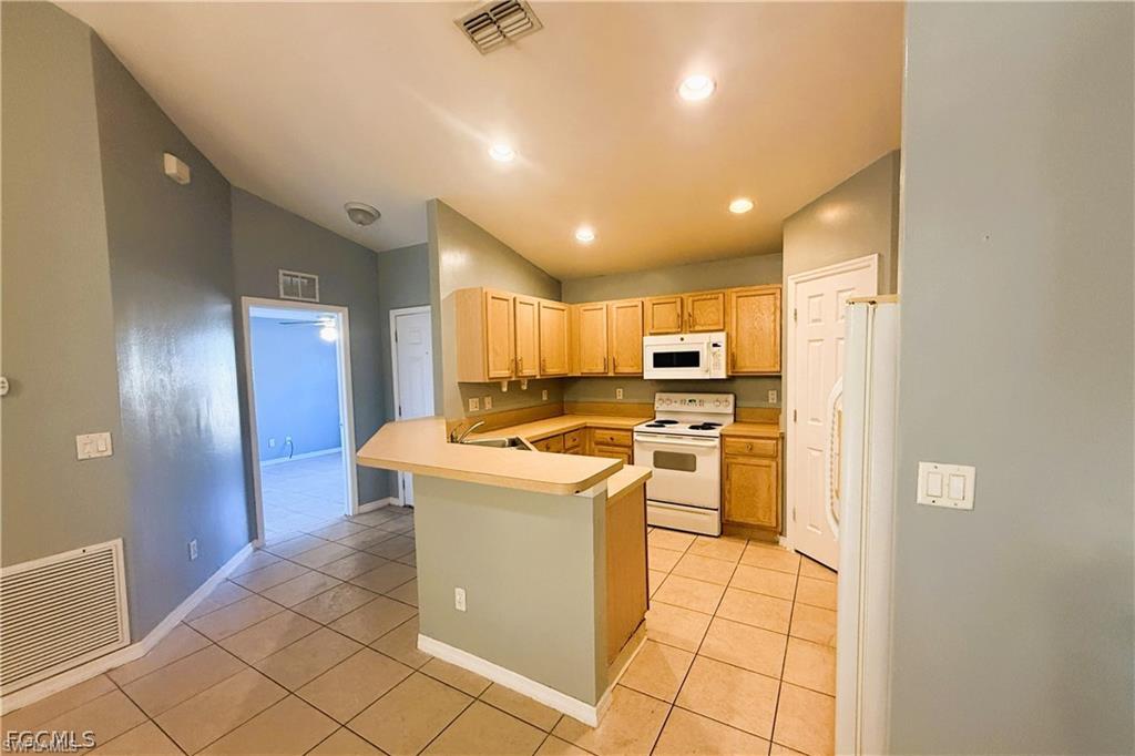 Kitchen with white appliances, light countertops, a peninsula, light tile patterned floors, and vaulted ceiling