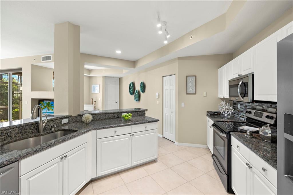 Kitchen featuring appliances with stainless steel finishes, a sink, white cabinets, decorative backsplash, and light tile patterned floors