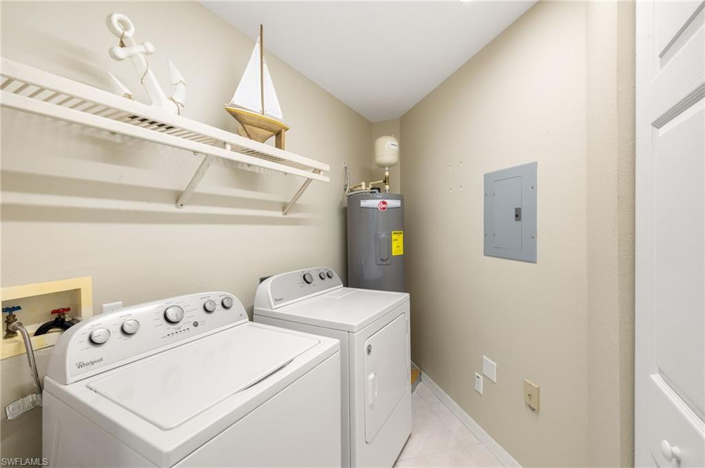 Laundry area featuring electric panel, electric water heater, washer and clothes dryer, light tile patterned floors, and baseboards
