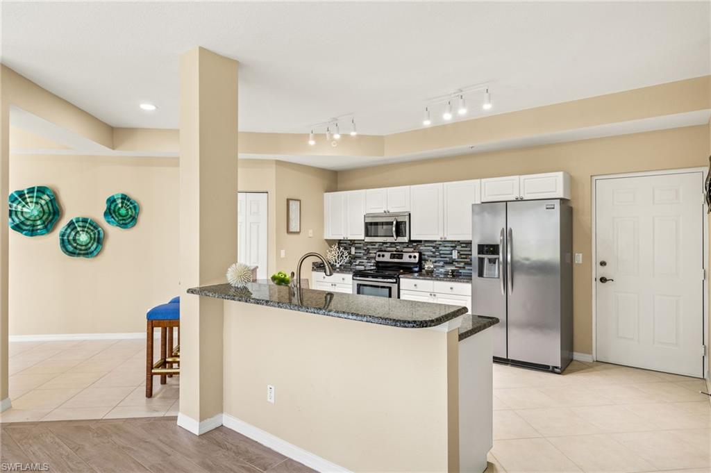 Kitchen featuring stainless steel appliances, dark stone counters, white cabinetry, and tasteful backsplash