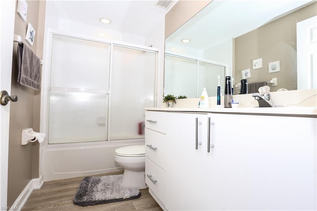 Full bath featuring vanity, light wood-type flooring, bath / shower combo with glass door, and recessed lighting