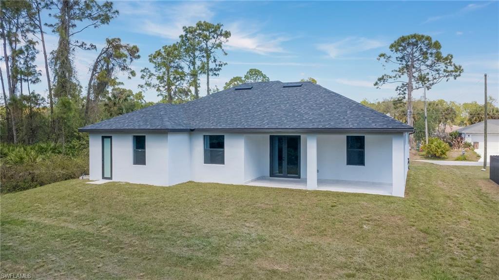 Back of property with a yard, stucco siding, roof with shingles, and a patio