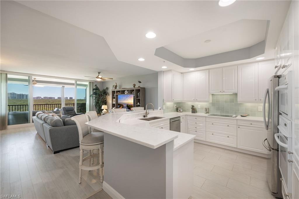 Kitchen with a kitchen bar, a peninsula, white cabinetry, tasteful backsplash, and light stone countertops