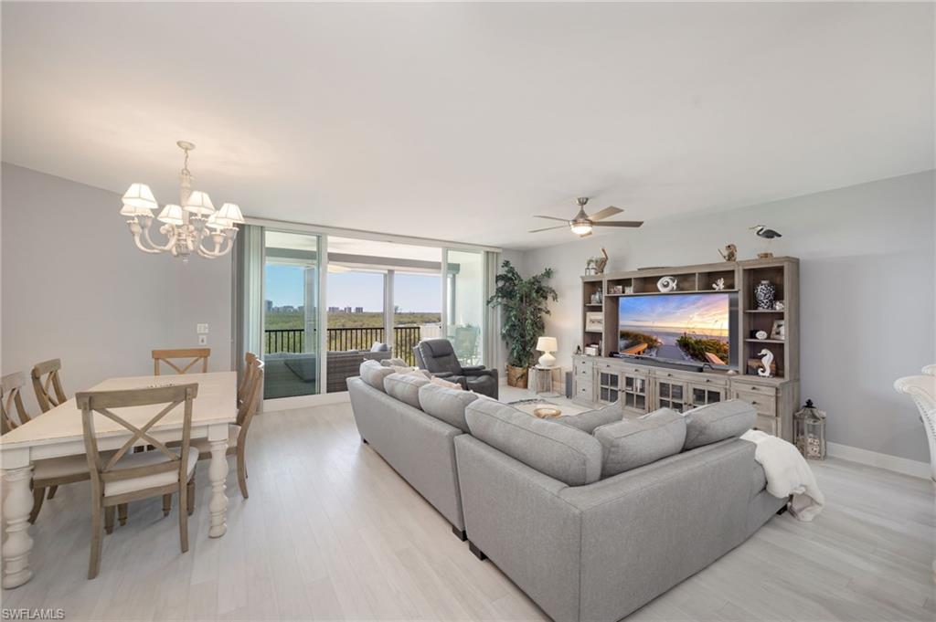 Living room with light wood finished floors, ceiling fan, a chandelier, and expansive windows