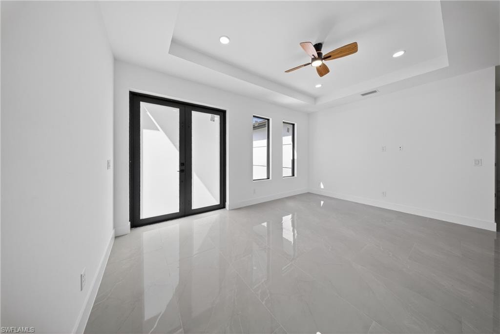 Empty room featuring ceiling fan, recessed lighting, french doors, light marble finish floors, and a raised ceiling