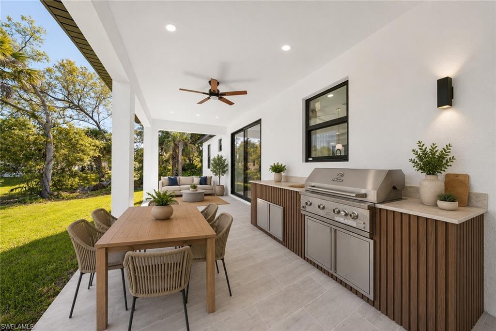 Covered outdoor living space featuring an integrated outdoor kitchen with a stainless steel grill, stone-look countertops, and wood-finish cabinetry