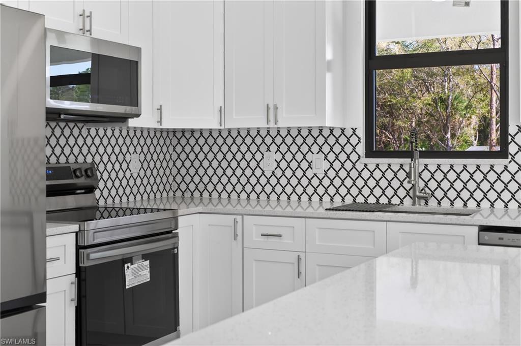 Kitchen with stainless steel appliances, white cabinetry, and light stone counters