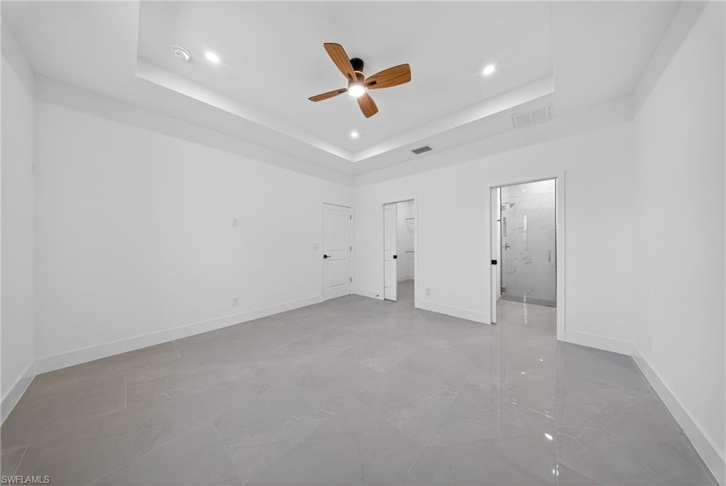 Unfurnished bedroom featuring ceiling fan, a tray ceiling, recessed lighting, light marble finish flooring, and a walk in closet