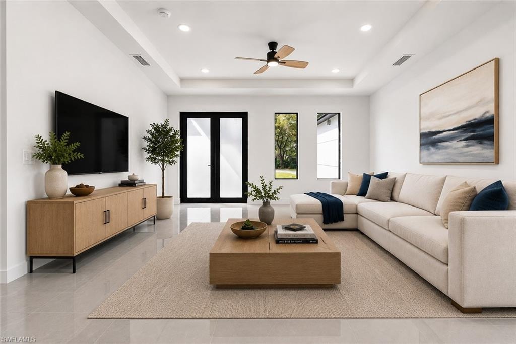 Spacious living area featuring light-toned flooring, a tray ceiling with recessed lighting and a ceiling fan, and black-framed double doors providing access