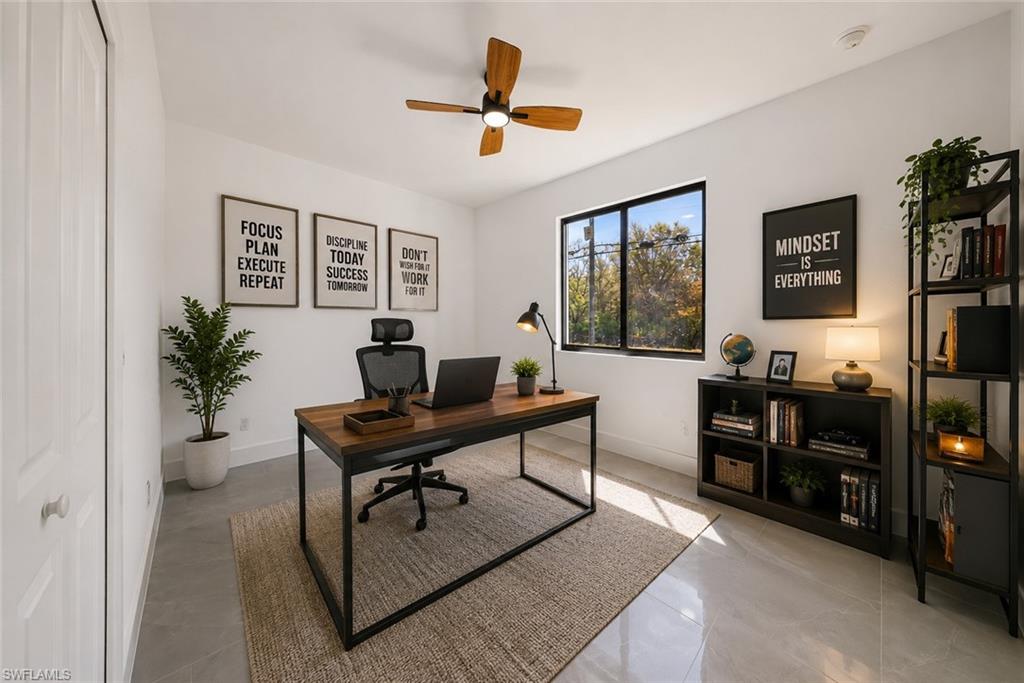 Dedicated workspace featuring a ceiling fan, a large window, a built-in closet with bifold doors, and light-toned tile flooring