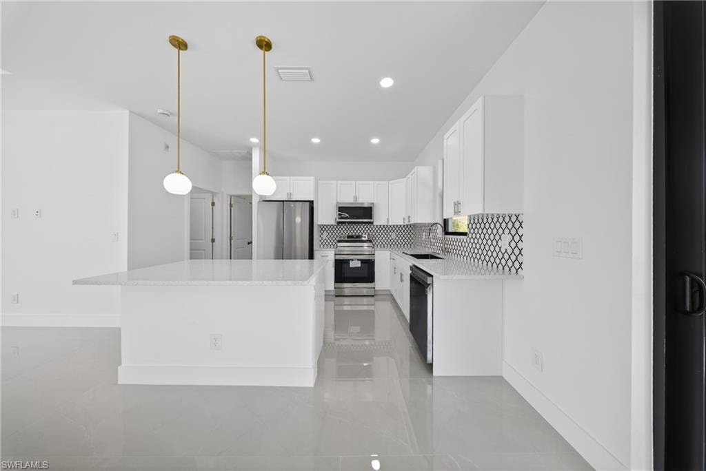 Kitchen with stainless steel appliances, white cabinets, tasteful backsplash, a center island, and light stone countertops