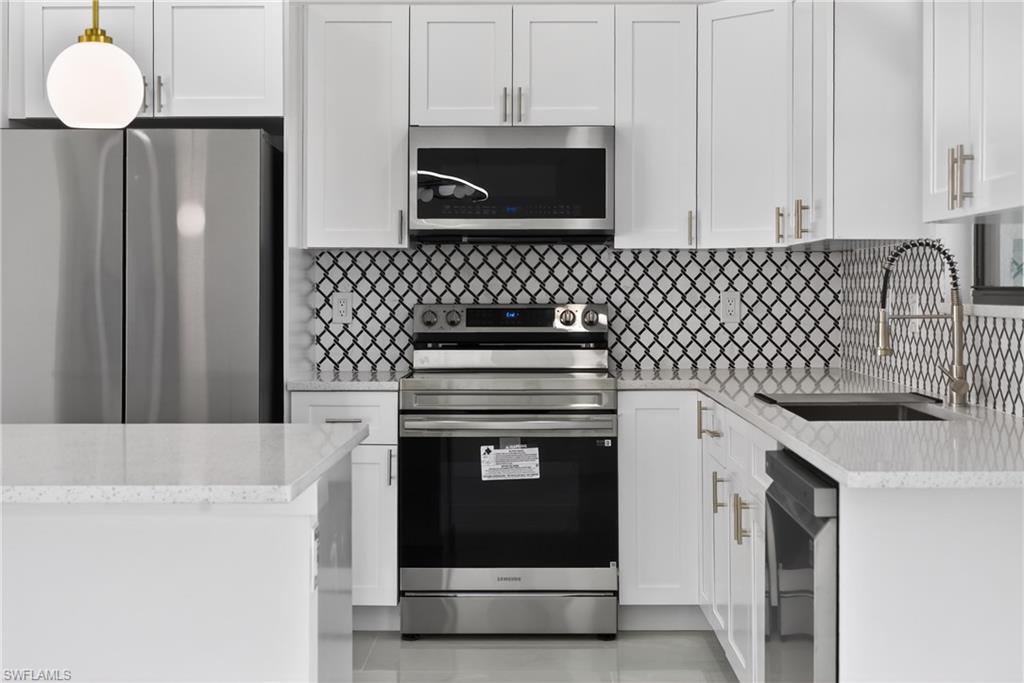 Kitchen with stainless steel appliances, white cabinets, light stone counters, and decorative backsplash
