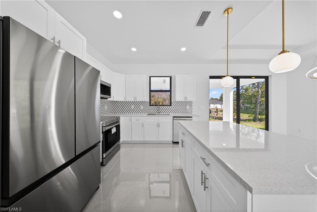Kitchen featuring stainless steel appliances, white cabinets, a center island, light stone countertops, and pendant lighting