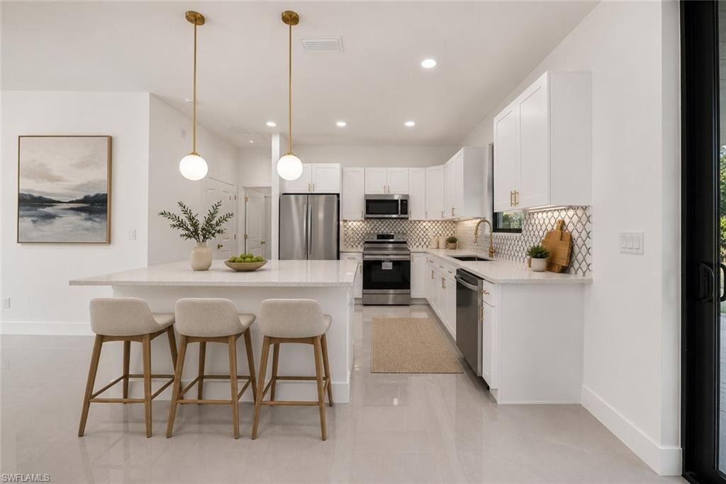 Contemporary kitchen featuring a large island with pendant lighting, white cabinetry, stainless steel appliances, and a decorative tile backsplash