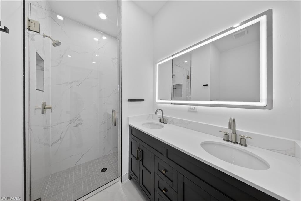 Full bathroom with double vanity, a marble finish shower, and recessed lighting