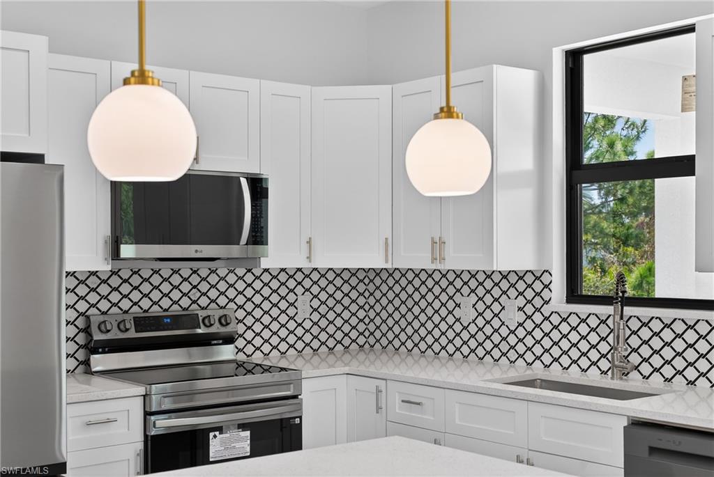 Kitchen featuring stainless steel appliances, white cabinetry, and light stone countertops