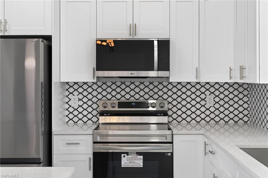 Kitchen with stainless steel appliances, white cabinets, light stone counters, and backsplash