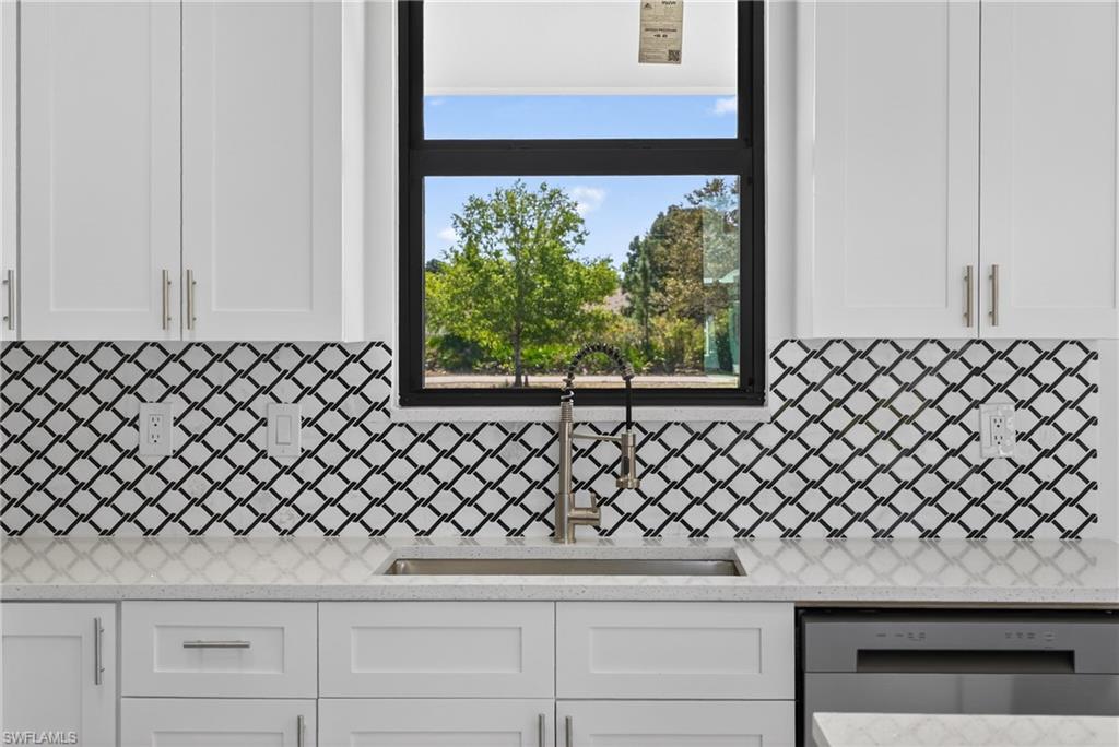 Kitchen featuring white cabinets, light stone countertops, and stainless steel dishwasher