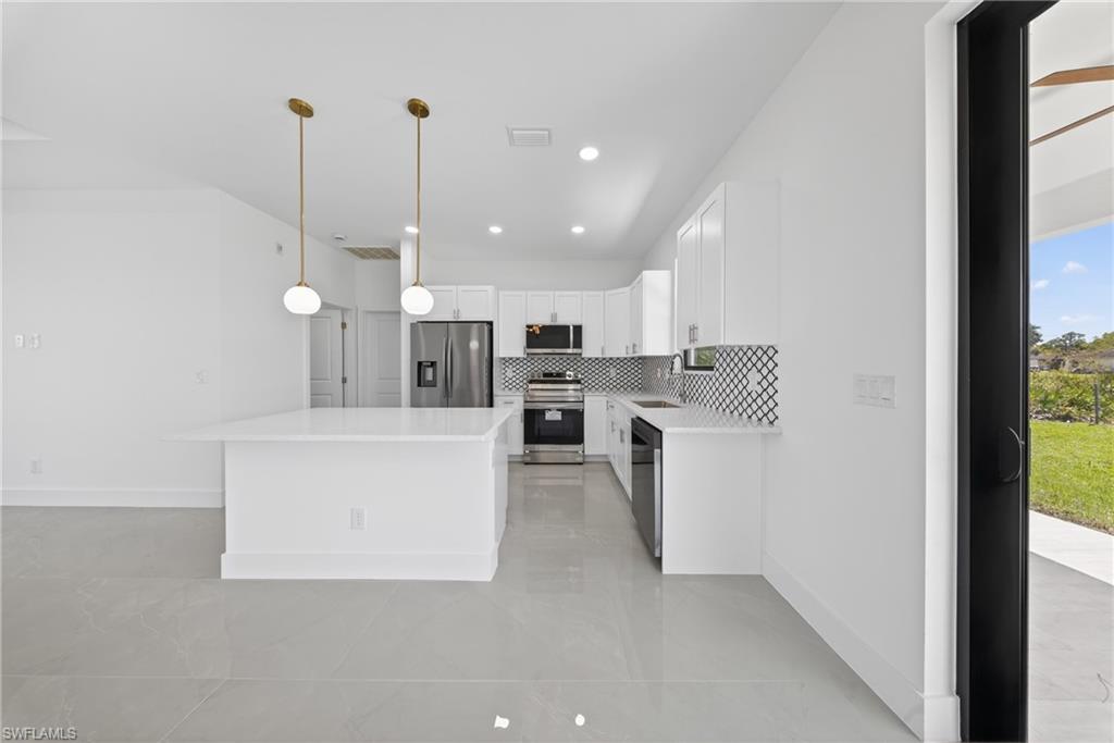 Kitchen featuring white cabinets, stainless steel appliances, a kitchen island, light stone countertops, and decorative backsplash