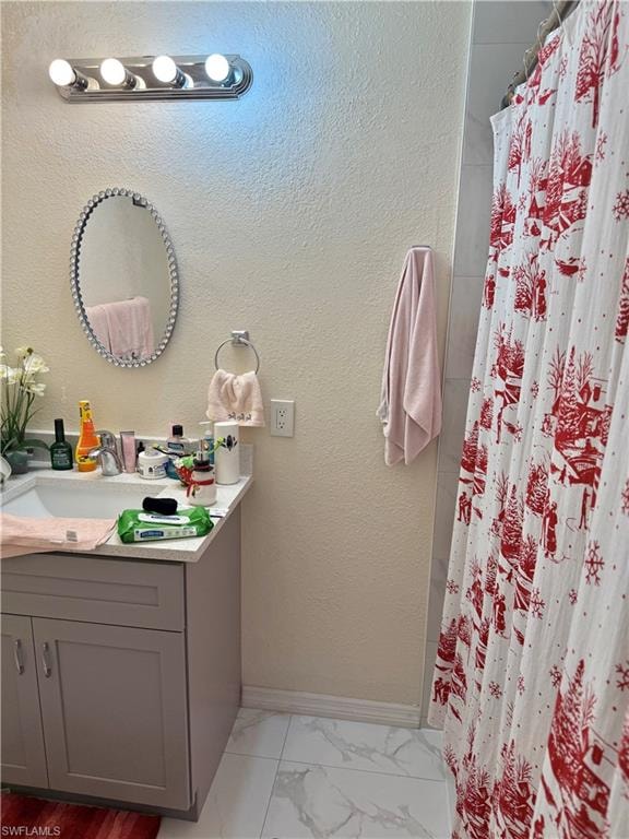 Full bath featuring vanity, curtained shower, a textured wall, and light marble finish floors