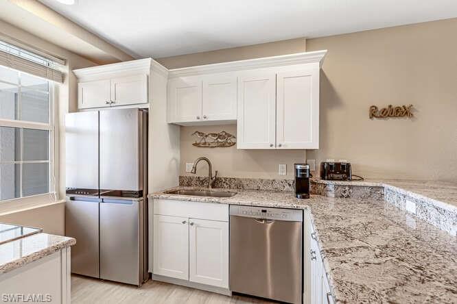 Kitchen featuring stainless steel appliances, white cabinetry, light stone countertops, and light wood-style floors