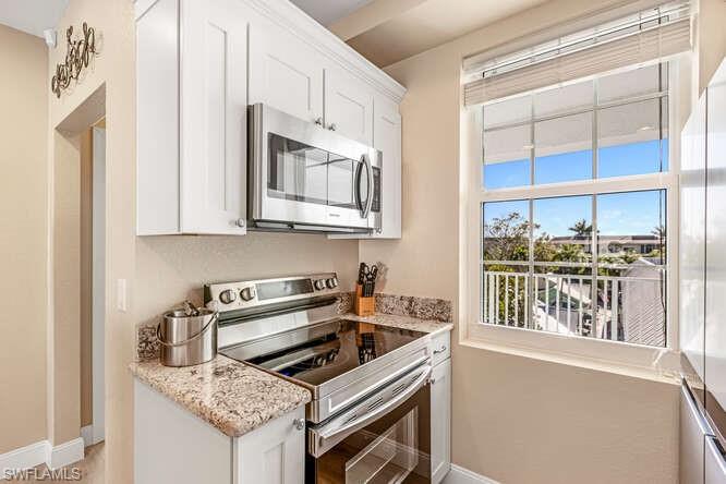 Kitchen with stainless steel appliances, white cabinetry, and light stone countertops