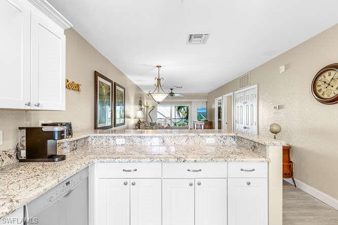Kitchen featuring white cabinetry, a peninsula, dishwasher, and light stone countertops
