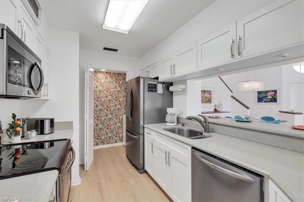 Kitchen featuring stainless steel appliances, white cabinetry, light wood-type flooring, and light stone counters