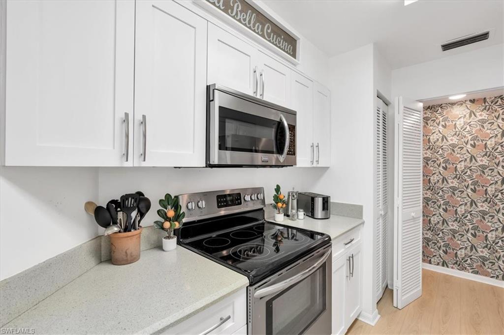 Kitchen with stainless steel appliances, white cabinetry, light stone counters, and light wood-style floors