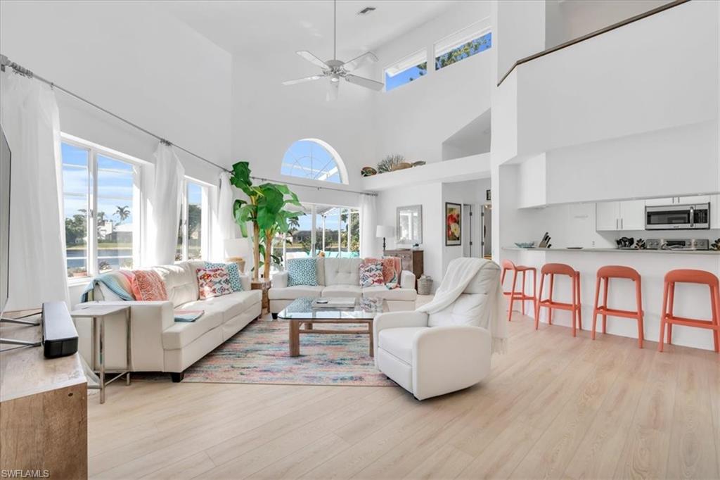 Living room with ceiling fan, a high ceiling, and light wood-type flooring