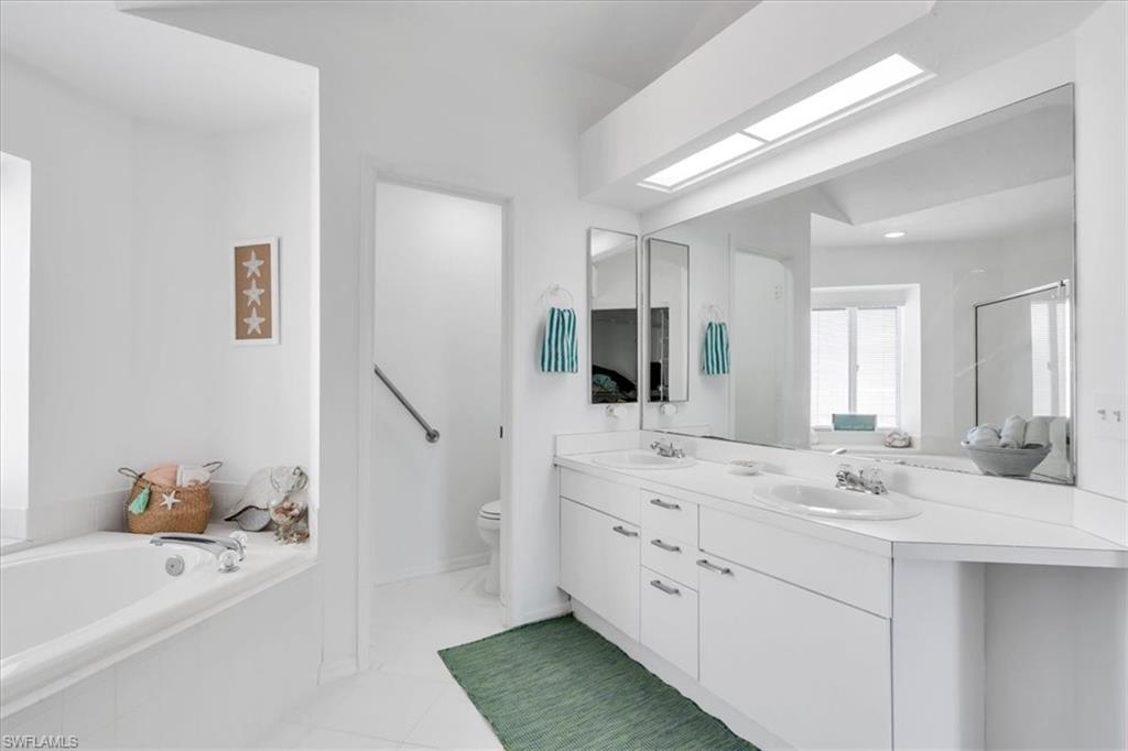 Bathroom featuring double vanity, a bath, a skylight, light tile patterned flooring, and a shower stall
