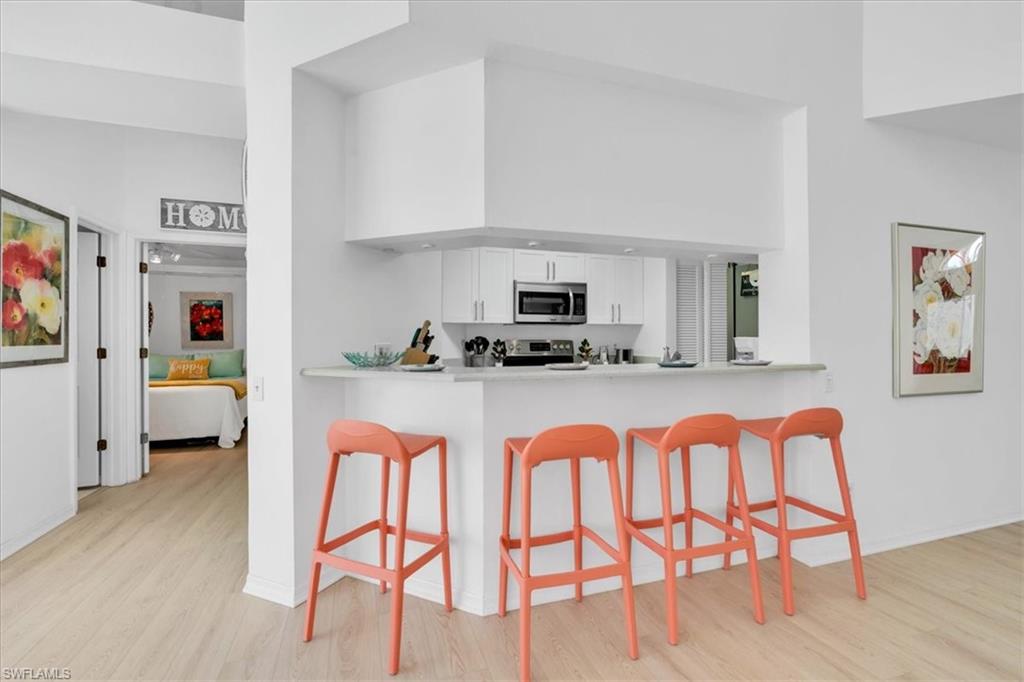 Kitchen featuring a high ceiling, a kitchen breakfast bar, light countertops, stainless steel appliances, and white cabinetry