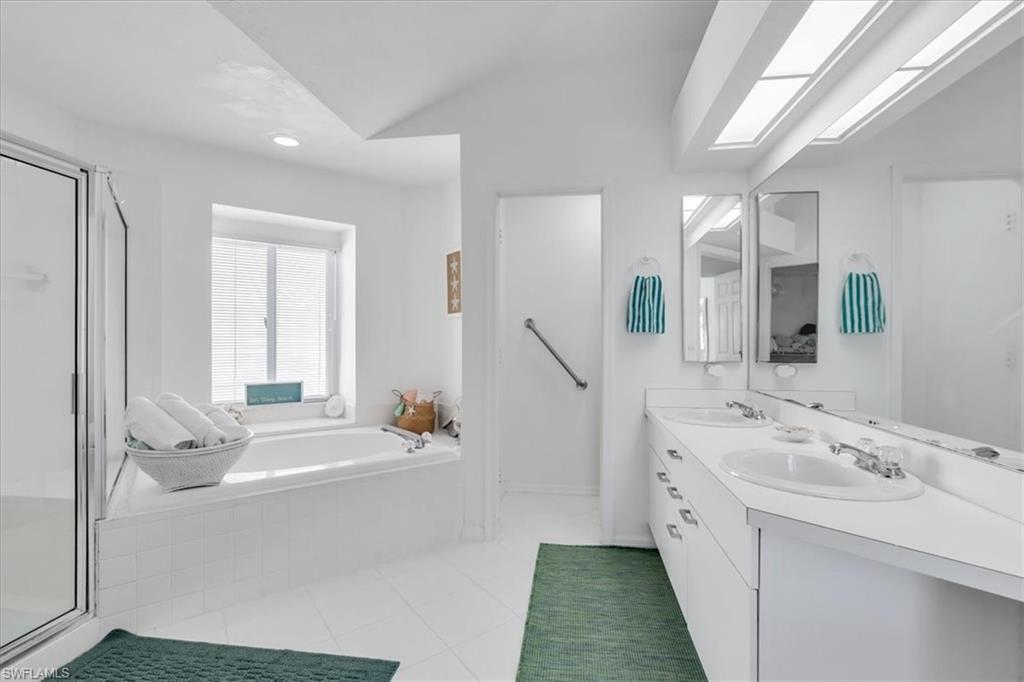 Full bath featuring double vanity, a shower stall, a garden tub, light tile patterned floors, and lofted ceiling