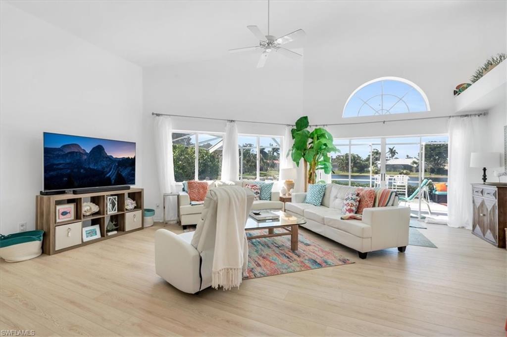 Living room with a high ceiling, a ceiling fan, and light wood-style floors