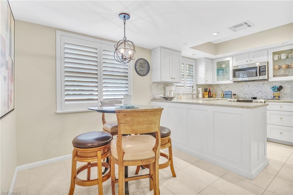 Kitchen featuring light stone countertops, glass insert cabinets, white cabinets, and stainless steel microwave