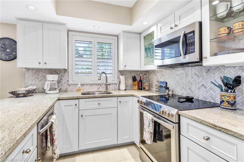 Kitchen with stainless steel appliances, white cabinetry, light stone counters, light tile patterned floors, and recessed lighting