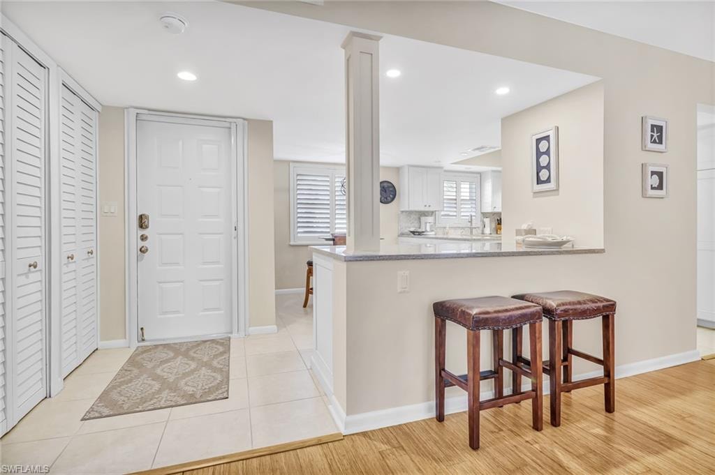 Kitchen with a kitchen bar, a peninsula, light stone counters, white cabinets, and recessed lighting