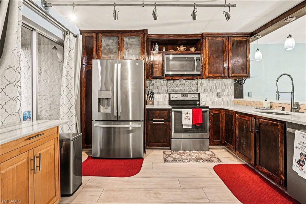 Kitchen featuring stainless steel appliances, backsplash, dark wood finish cabinetry, light stone counters, and rail lighting
