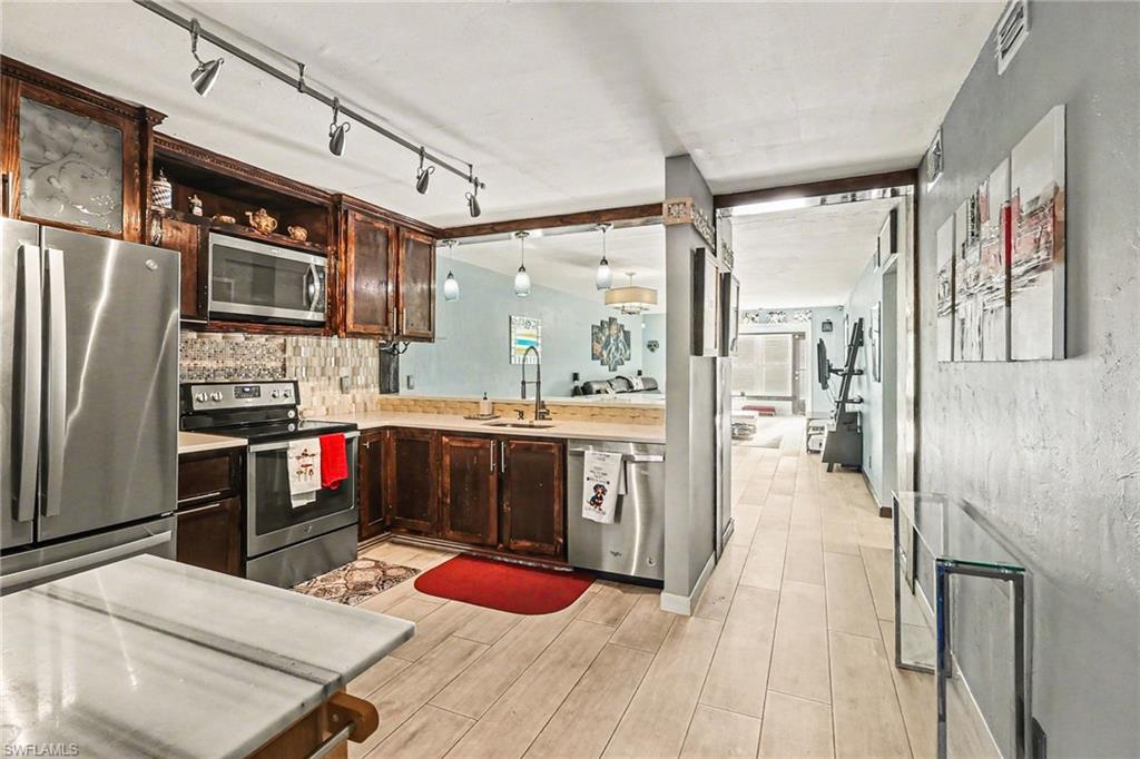 Kitchen featuring stainless steel appliances, dark wood finish cabinetry, wood tiled floors, decorative backsplash, and track lighting