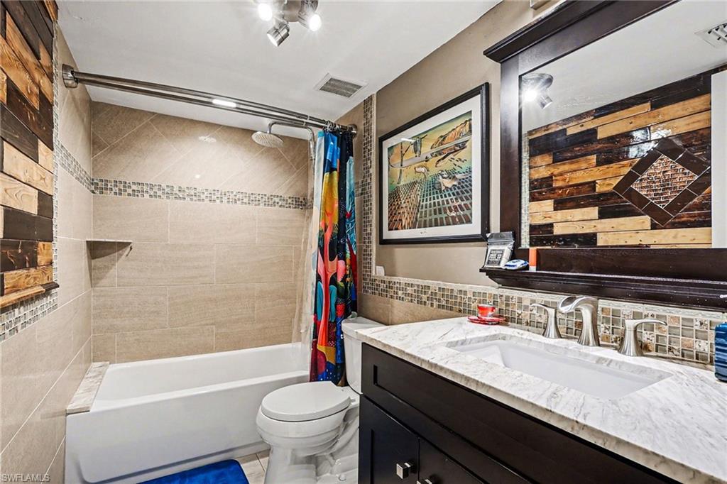 Bathroom featuring vanity, shower / bath combo with shower curtain, and tile walls