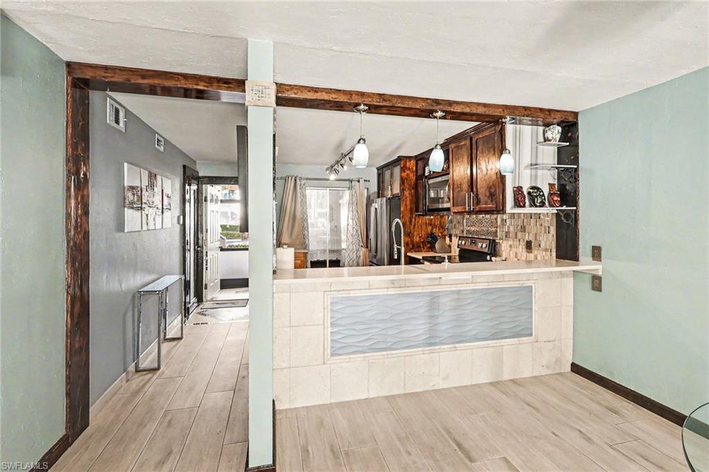 Kitchen with wood finish floors, stainless steel appliances, light countertops, beam ceiling, and decorative backsplash