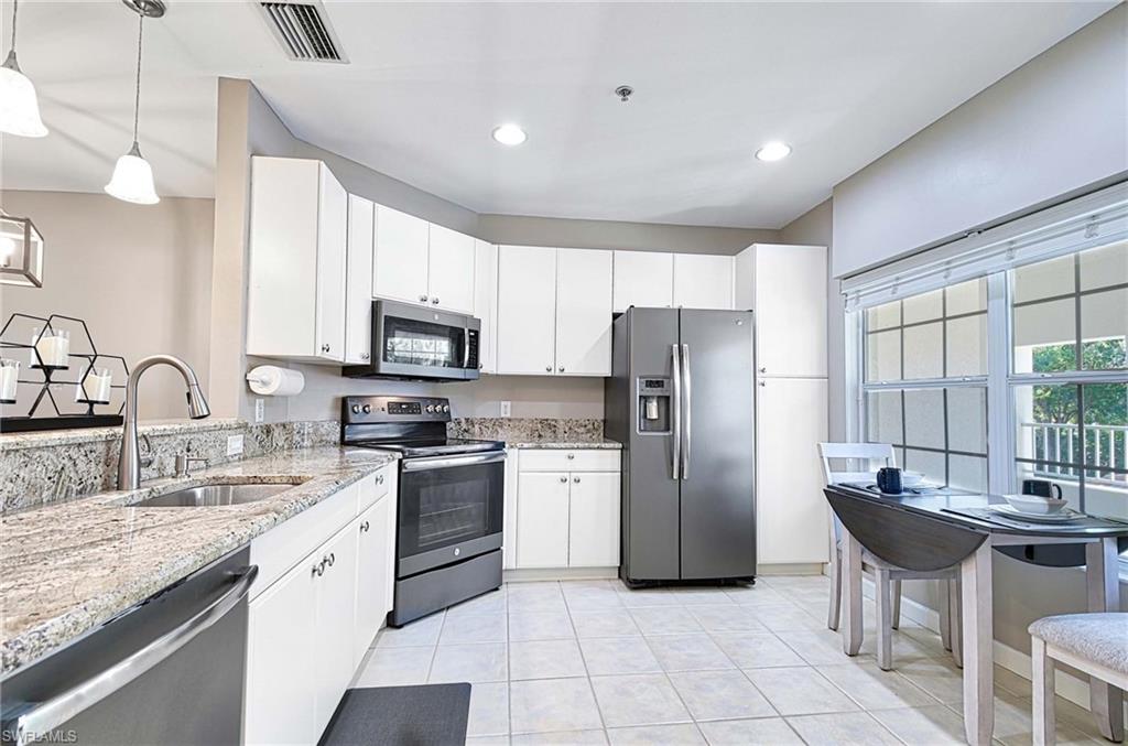 Kitchen featuring stainless steel appliances, light stone counters, hanging light fixtures, white cabinets, and light tile patterned floors