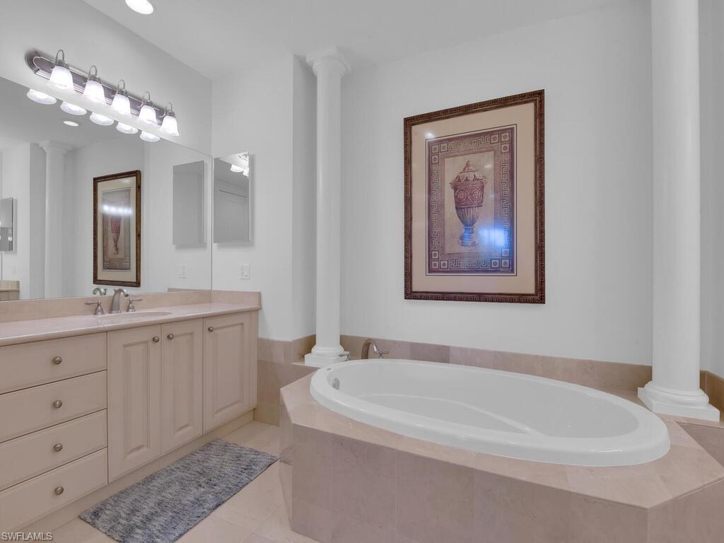 Full bath featuring tile patterned floors, decorative columns, vanity, and a bath
