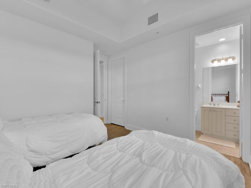Bedroom featuring ensuite bathroom, baseboards, light wood-style flooring, and visible vents
