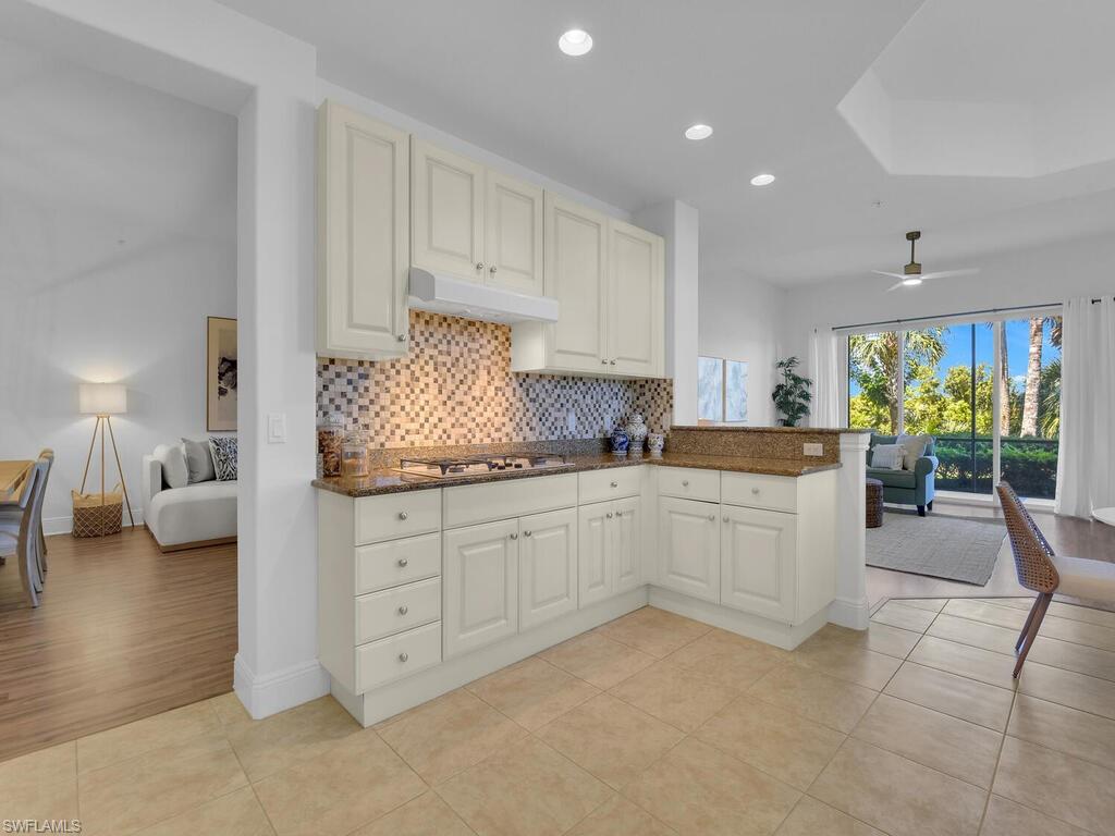 Kitchen with stainless steel gas stovetop, decorative backsplash, dark stone counters, under cabinet range hood, and open floor plan
