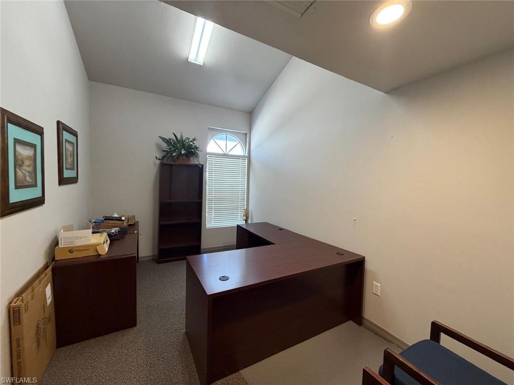 Office space with lofted ceiling and dark colored carpet