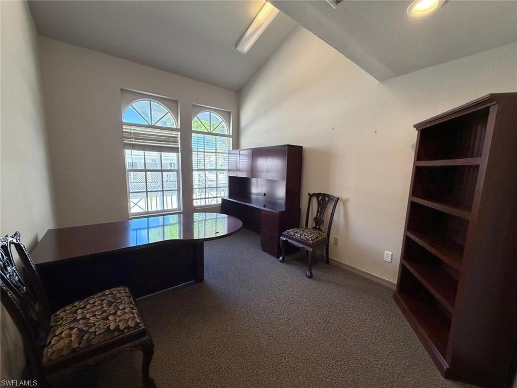 Home office with vaulted ceiling and dark carpet