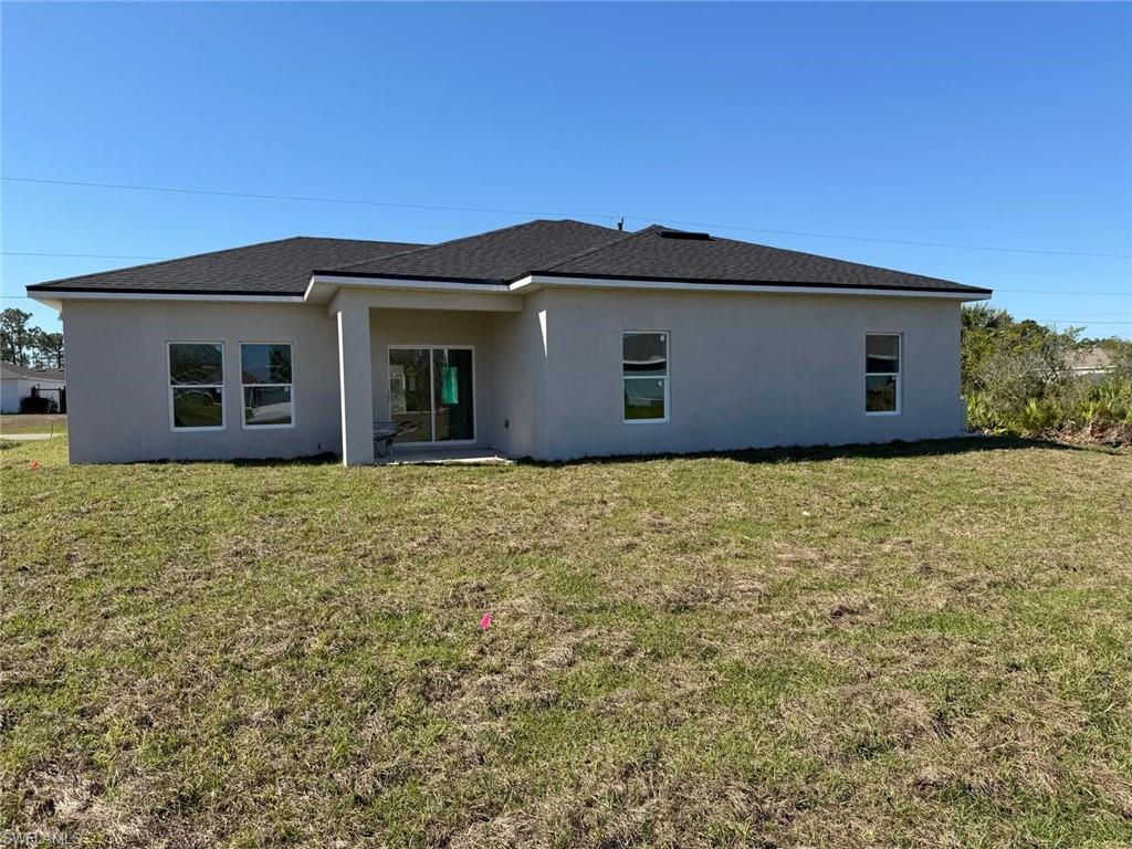 Back of house with a yard, stucco siding, a patio, and a shingled roof