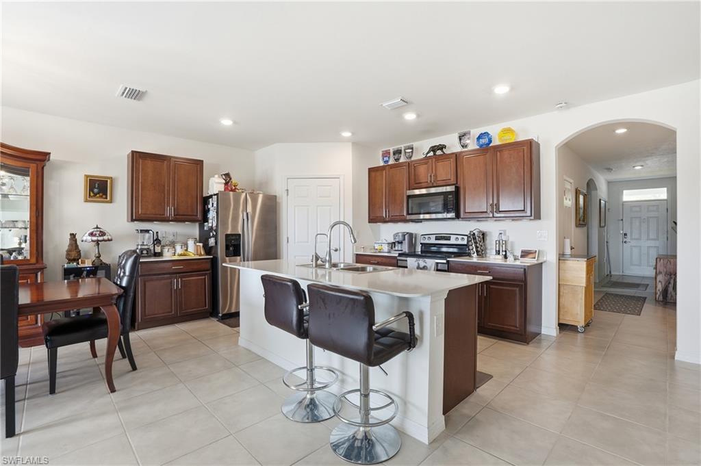 Kitchen with arched walkways, a breakfast bar area, stainless steel appliances, a center island with sink, and light tile patterned flooring