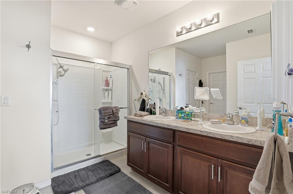 Full bath featuring double vanity, a shower stall, and light tile patterned floors